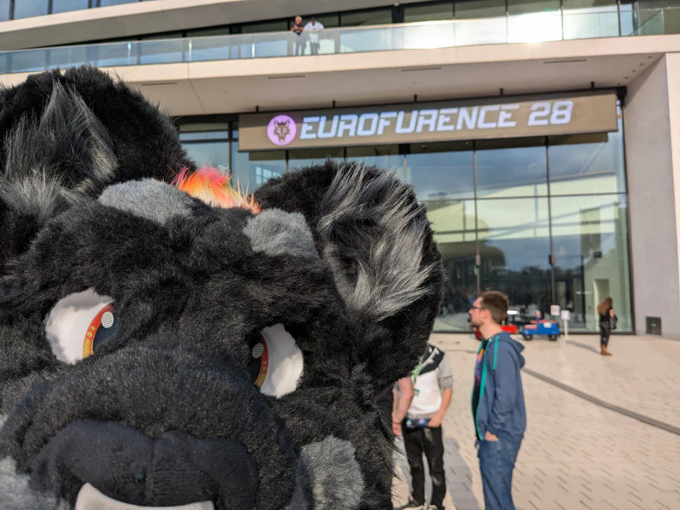 Photo from the Eurofurence registration queue, with the EF sign in the background and my fursuit head close up looking at the camera"