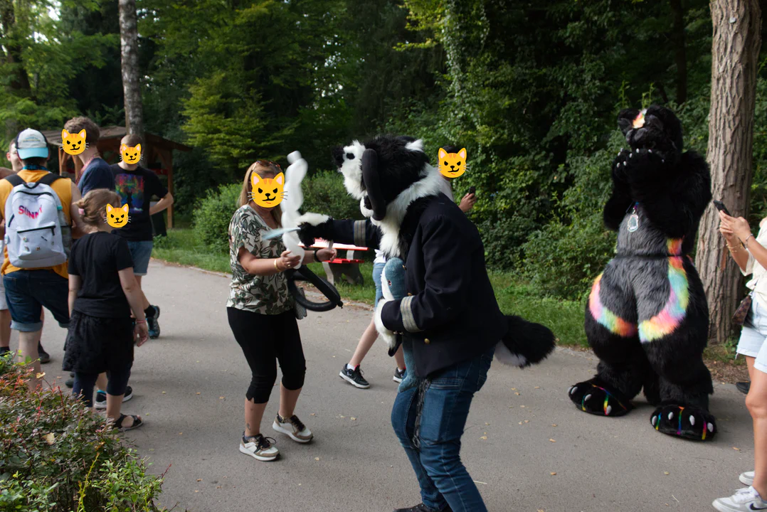 A black and white demon dog fursuiter holding a plush sword, fencing playfully with a guest holding a long balloon